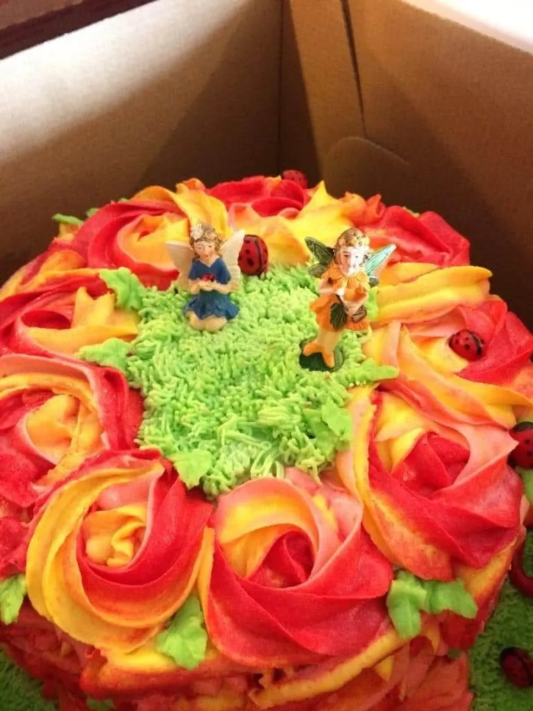 Hand-piped floral birthday cake with red and yellow rosettes, fairy toppers, and ladybug details baked in Peebles Ohio